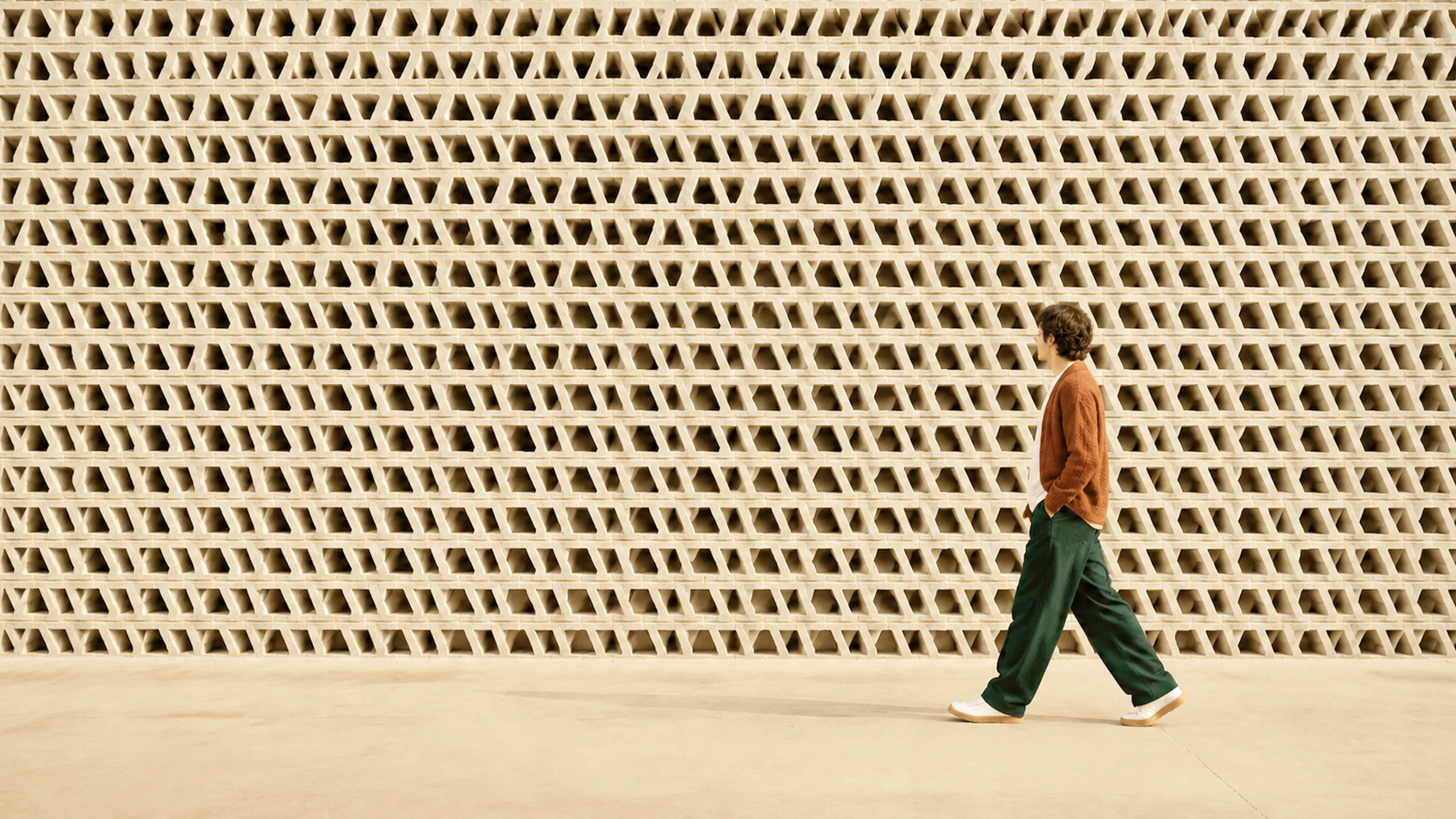 A man walking past a textured breeze-block wall.